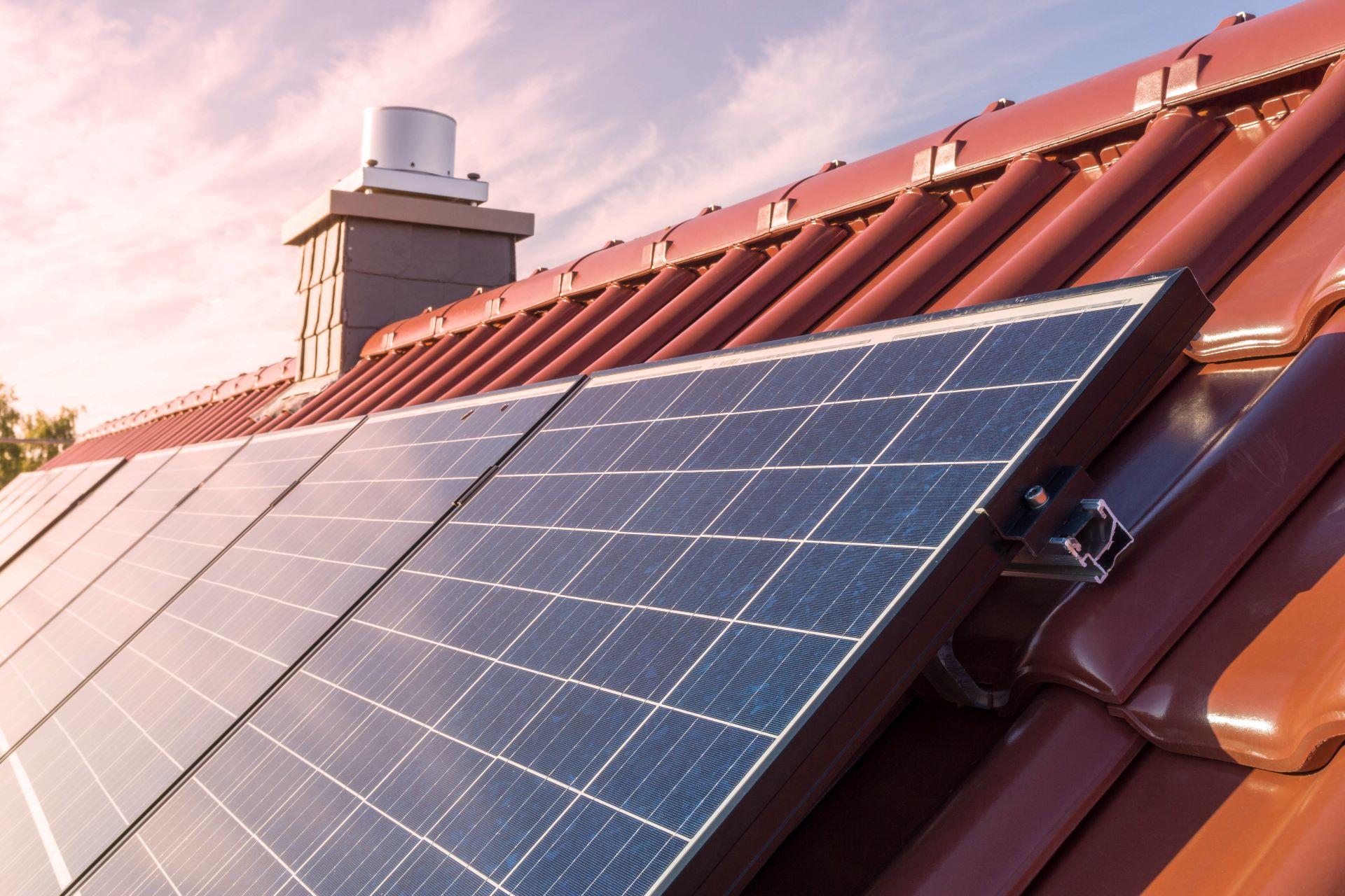 Solarmodule auf einem roten Ziegeldach, die in der sanften Morgensonne glänzen. Der Kamin im Hintergrund deutet auf ein Wohngebäude hin.