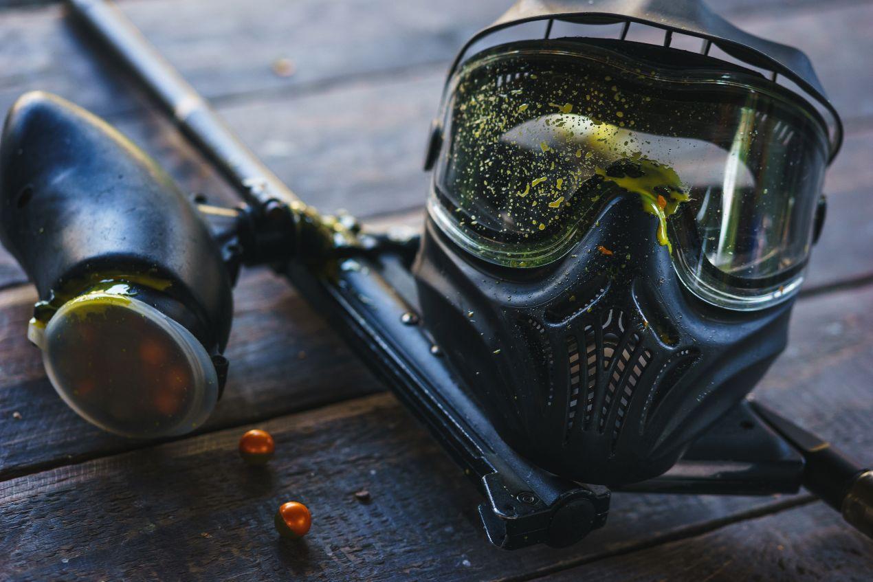 Schutzmaske und Paintball-Markierer mit Farbresten auf Holzuntergrund – zeigt realen Zustand von Druckluftwaffen nach Nutzung