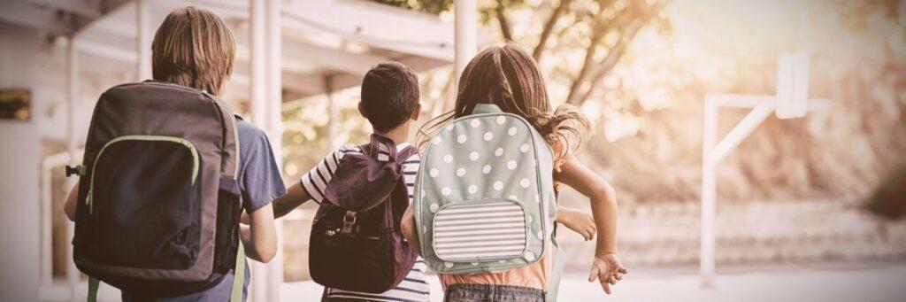 Drei Kinder mit Schulrucksaecken laufen auf einen Schulhof – typischer Alltag an einer Berlin Privatschule